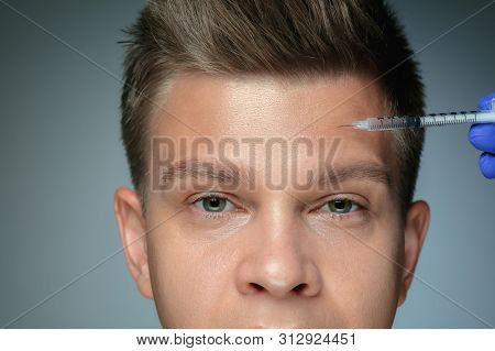 Close-up Portrait Of Young Man Isolated On Grey Studio Background. Filling Surgery Procedure, Forehe