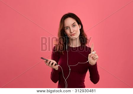 Portrait Of A Pretty Brunette Girl Holding Earphone In One Hand And Mobile Phone In Another One Expr