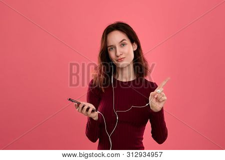 Portrait Of A Pretty Brunette Girl Holding Earphone In One Hand And Mobile Phone In Another One Expr