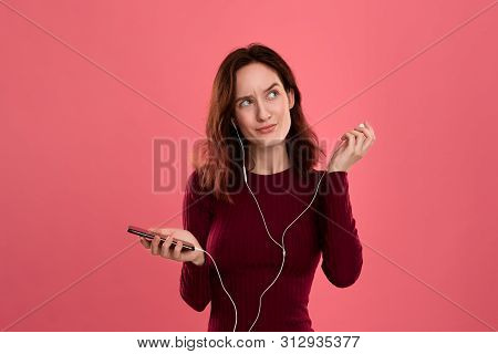 Portrait Of A Pretty Brunette Girl Holding Earphone In One Hand And Mobile Phone In Another One Expr