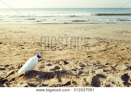 White Plastic Bottle Lying On The Shore Of The Beach And Pollutes The Sea And The Marine Life, Conce