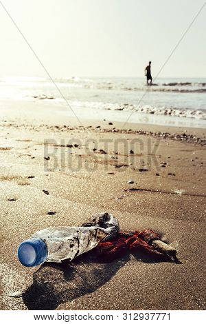 Vertical Photo Of A Plastic Bottle And Garbage Lying On The Shore Of The Beach Polluting The Sea And