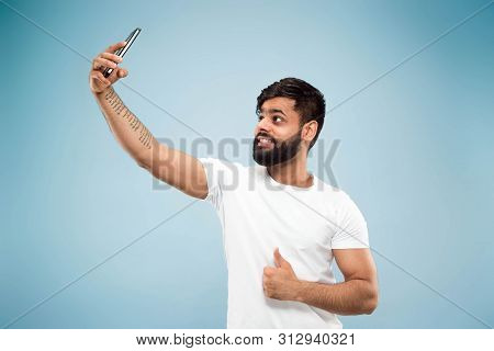 Half-length Close Up Portrait Of Young Hindoo Man In White Shirt On Blue Background. Human Emotions,