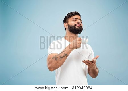 Half-length Close Up Portrait Of Young Hindoo Man In White Shirt On Blue Background. Human Emotions,