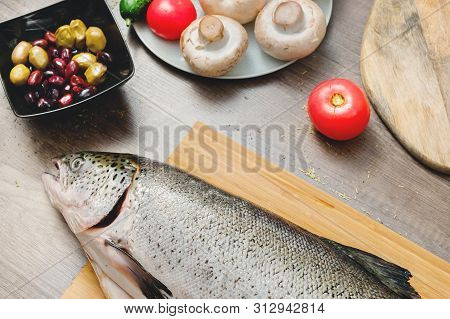 Close-up Keta Fish, Whole On The Cutting Board Of The Kitchen Table Next To Olives Tomatoes And Mush