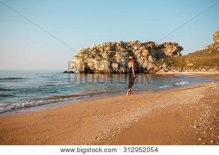 Portrait Of A Girl In A Black Dress And Hat On The Beach