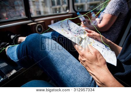 closeup of a young cacausian man traveling on an open top tour bus, checking a city map and using earphones, with a sunbeam in the background