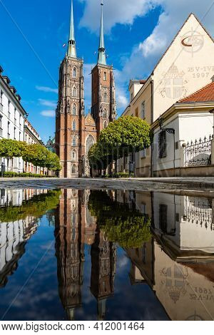 Wroclaw, Poland - May 3 2020: Facade Of Cathedral Of St. John The Baptist Reflected In Puddle