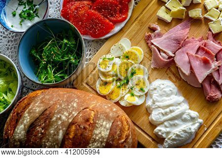 Continental, healthy breakfast containing homemade bread, vegetables tomatoes, argula, sald, cheese burratta, camembert, ham and egg. 