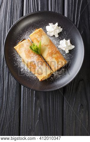 Delicious Crepes With Apricot Jam, Whipped Cream And Powdered Sugar Close-up In A Plate On The Table