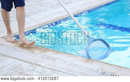 Man Cleaning A Swimming Pool In Summer With A Brush Or Net On A Blue Pole Standing Barefoot On The T