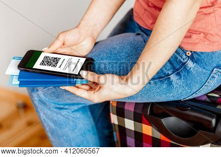 The woman holding the mobile phone a mockup for digital vaccination certificate in one hand and passport, mask and ticket in another one