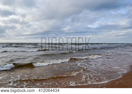 Seascape In Summer With Kitesurfers And Green Sails. Cloudy Dramatic Skies And Waves Washing The Bea