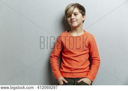 A Smiling Boy 9 Years Old With A Fashionable Hairstyle In An Orange Sweater Looks To The Side. Grey 