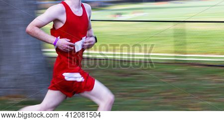 Panning To Add Blurred Motion To Runner Racing In A Red Uniform Passing A Tree With A Black Fence An