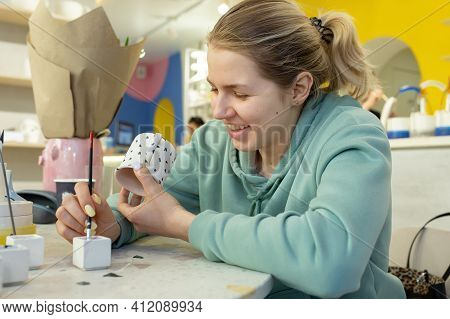 Smiling Young Woman In Casual Clothes Maks Ornament On Teecup In A Ceramic Workshop. Learning New Sk