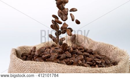 Falling Roasted Coffee Beans in jute bag. White background, close-up.