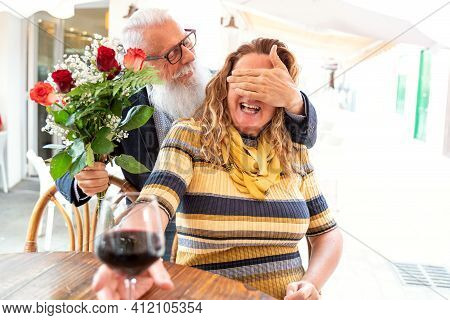 Beautiful Happy Senior Couple On A Romantic Date In Restaurant. Handsome Man With White Beard Surpri
