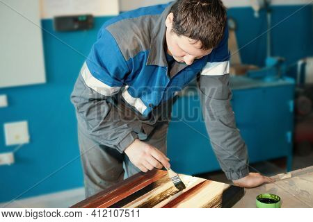 A Working Cabinetmaker Holds A Brush In His Hand And Paints A Wooden Surface. A Trace Of Paint On A 
