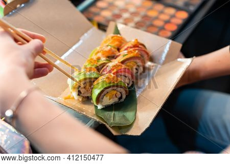 Close Up Of Chopsticks Taking Portion Of Sushi Roll On The Table Restaurant. Eating Sushi Roll Using