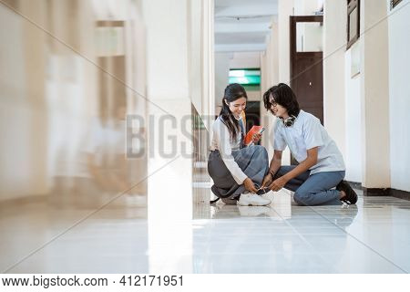 A Boy In Glasses With Headphones And A Girl In A High School Uniform Clumsily Tying Shoelaces Togeth