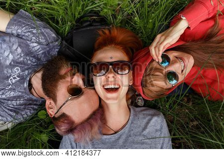 Top View Of A Smiling Enjoying Young People In Sunglasses, Lying Down On A Green Grass, In The Park,