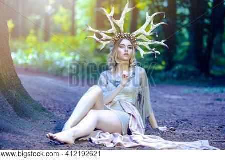 Portrait Of Beautiful Girl Posing With Artistic Deer Horns In Summer Forest On Sandy Forest Ground W