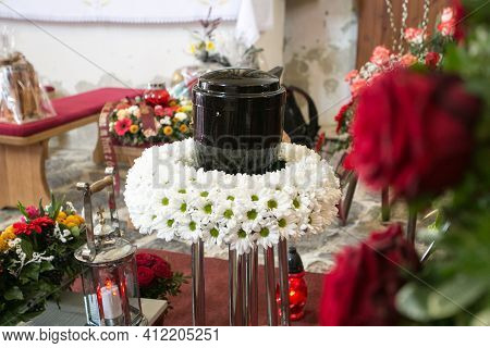 Black Urn On The Funeral Day In Church; Surrounded With Daisies And Roses
