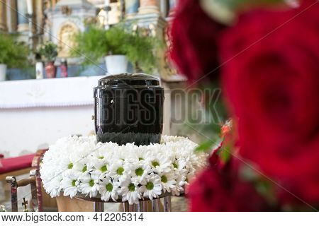 Black Urn On The Funeral Day In Church; Surrounded With Daisies And Roses