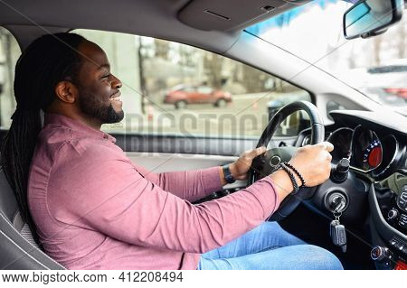 A Happy African-american Man With The Dreadlocks Is Driving A Car, Side View From A Passenger Seat O