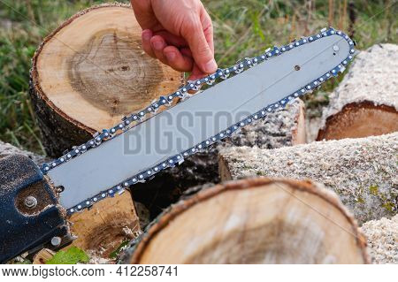 Checking And Adjusting The Chain Tension Of The Chain Saw. A Worker Checks The Tension Of The Saw Ch