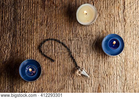 The Pendulum On A Chain With A Natural Crystal On A Background Of Wood Texture With Three Burning Ca