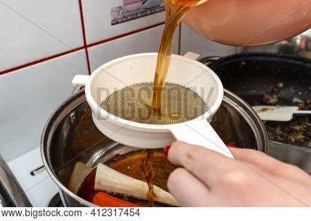 The Woman Pours The Decoction Of The Mushroom Soup Through A Plastic Strainer.
