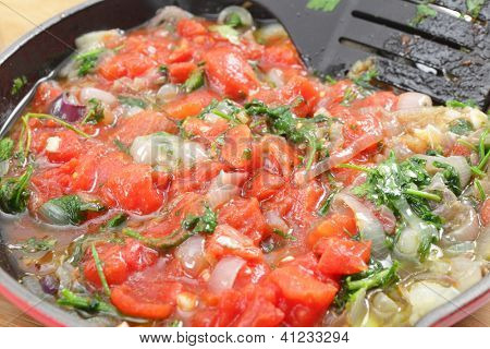 Stegte løg og persille og tomater i en gryde, en del af forberedelserne til en græsk udstoppede aubergine