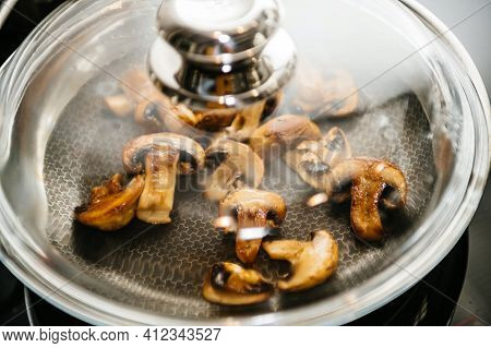 Macro Close-up Of Frying Pan Covered With Glass Lid Of Fresh Mushrooms Being Fried