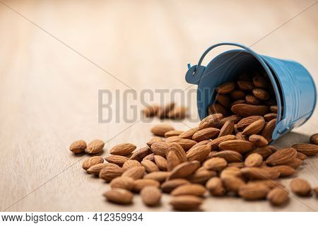 Almonds Pour From Blue Bucket
 On Wooden Table. Almond Concept With Copyspace.