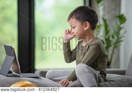 Asian Boy Looking At The Tablet Screen Attentively. Overstimulated Children Concept. Too Much Screen