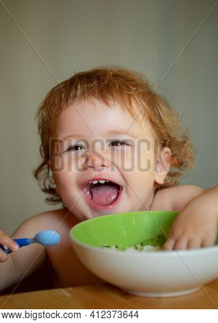 Smiling Baby Eating Food. Cutr Baby Child Eating Himself With A Spoon. Launching Child Eating Food