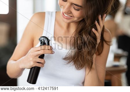 Happy Woman Spraying Hairspray Styling Wavy Hair In Bathroom, Cropped