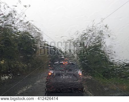 Rain Falls On The Windshield Of A Car. Raindrops From Inside The Vehicle. The Taillights Of A Car Se