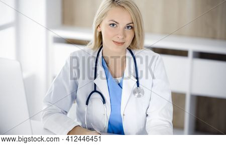 Portrate Of Woman-doctor At Work While Sitting At The Desk In Clinic. Blonde Cheerful Physician Read