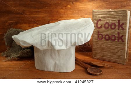 Chef's hat med skedar och kokbok på trä bakgrund