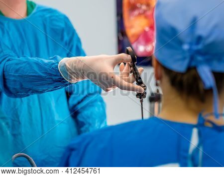 The Surgeons Hands In Latex Gloves And Blue Uniforms Hold Special Medical Instruments During Laparos