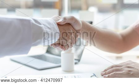 Two men holding hands, Asian doctor smiled shake hands with the patient congratulating him on being 