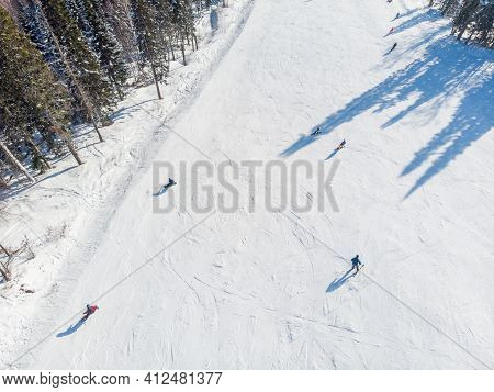 Snowboarders And Skiers Drive Down Ski Slope In Winter Through Fresh Snow, Areal Top View