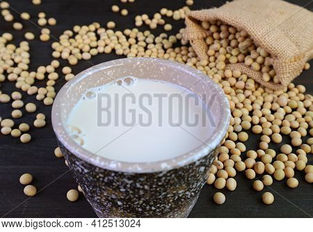 Cup Of Soy Milk Isolated On The Table With Blurry Soybeans Scattered From Burlap Bag