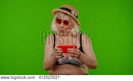 Senior Old Exited Woman Tourist In Swimsuit Playing Video Game On Mobile Cell Phone On Chroma Key