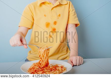 Cute Boy Eating Spaghetti Bolognese At Home. Concept Of Dirty Stains On Clothes. Isolated On Blue Ba