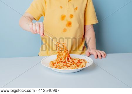 Cute Boy Eating Spaghetti Bolognese At Home. Concept Of Dirty Stains On Clothes. Isolated On Blue Ba