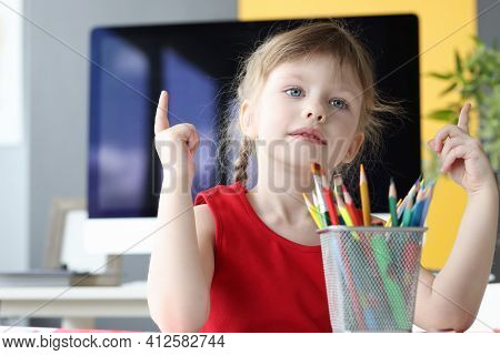 Little Girl Sits At Table With Pencils And Counts Numbers On Her Fingers